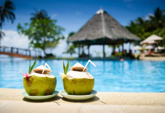 Two green coconuts hold delicious drinks perfect for poolside relaxation at a tropical resort surrounded by palm trees.