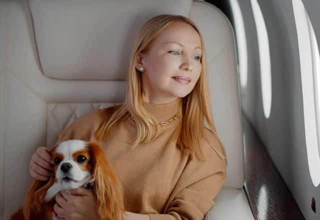 A woman sits on a private jet with her pet dog