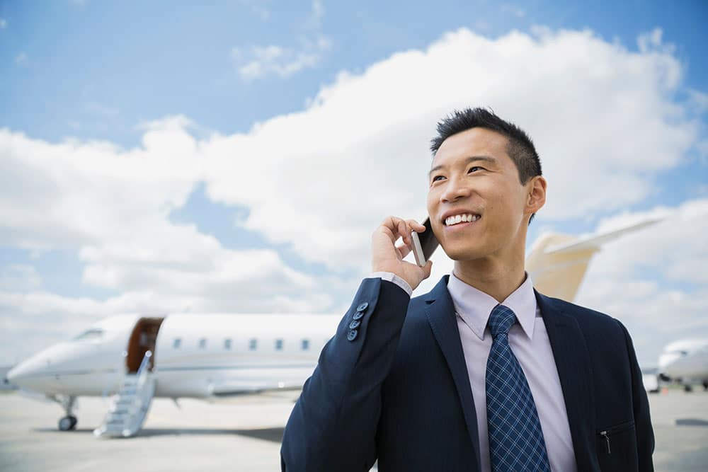 A man standing next to a private jet while on his phone