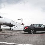 A car on the tarmac next to a private jet