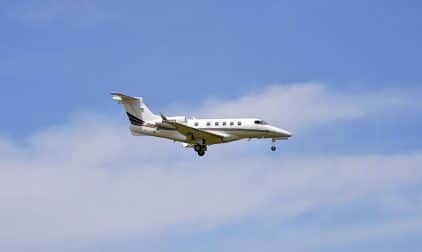 A private jet with wheels down approaches a runway.