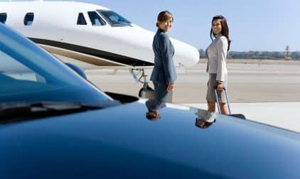 Two travelers approach a private jet on the runway.