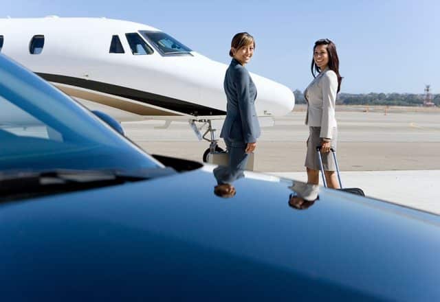 Two travelers approach a private jet on the runway.